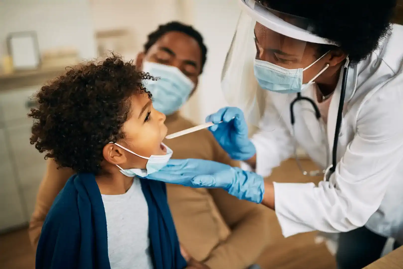 female doctor with tongue depressor for child opening mouth